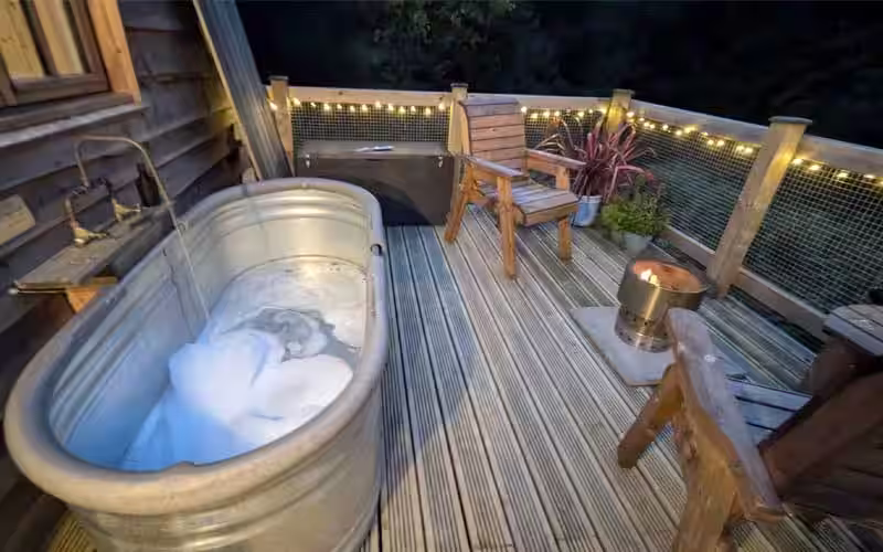 Outdoor bath running, with bubbles on decking, next to burning firepit - a digital detox.